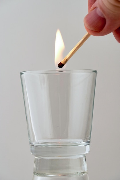 Hand holds a burning match over a transparent glass