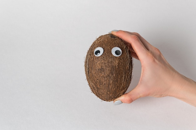 Hand holds the coconut with Googly eyes on white background. coconut character with funny face