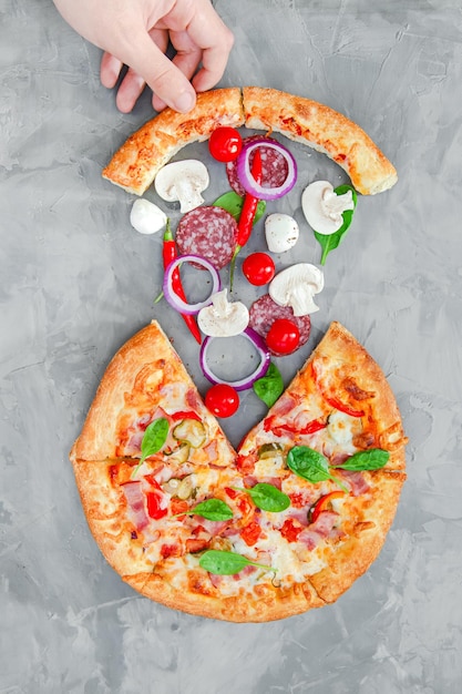 Hand holds a cut piece of pizza on a gray background