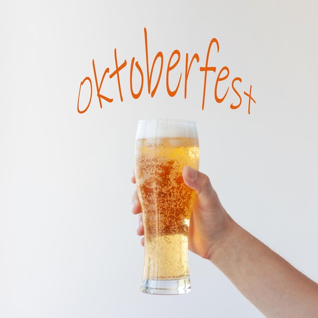 A hand holds a full glass of light beer with bubbles and foam on a white background