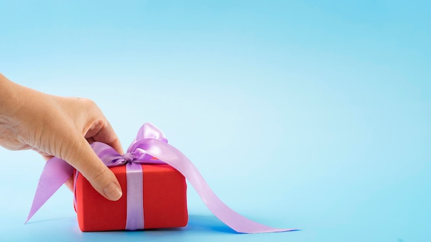 A hand holds for a gift in a red wrapping bag with a ribbon on a blue background.