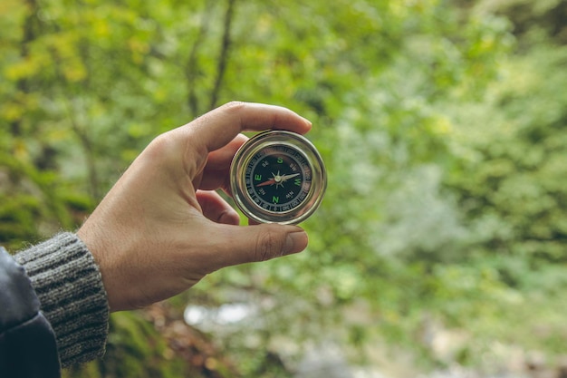 Hand holds golden compass on forest background