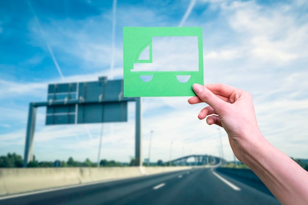 Hand holds green logistics symbol against highway