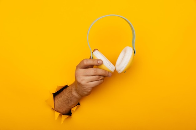 Hand holds headphones through a hole of yellow background