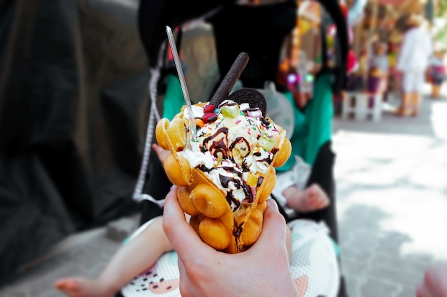 Hand holds a Hong Kong waffle dessert Sweets with ice cream cookies syrup and sweets