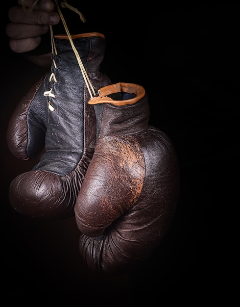 Hand holds a pair of brown very old boxing gloves 