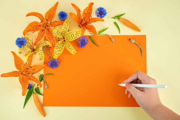 Photo hand holds a pen and writes congratulations beautiful flowers on a yelloworange background