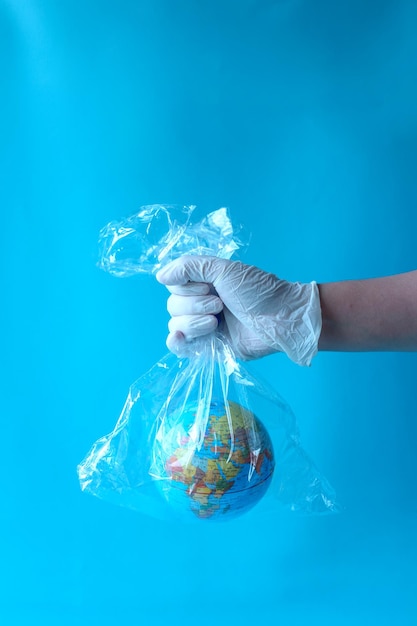 Hand holds plastic bag using hand glove with planet earth globe in blue background. The concept of p