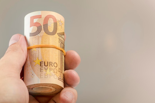 The hand holds a roll of 50 euro banknotes Euro banknotes rolled up in a white man's hand on a gray background The concept of financial assistance real estate purchase loan or insurance payment