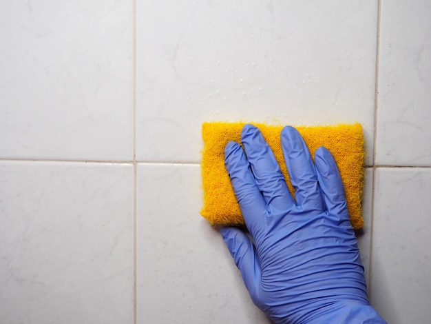 Hand holds a sponge against a tiled wall