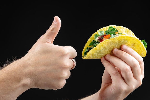 A hand holds a taco with vegetables and a black background isolate empty space for text clean eating