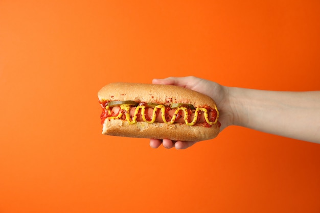 Hand holds tasty hot dog on orange