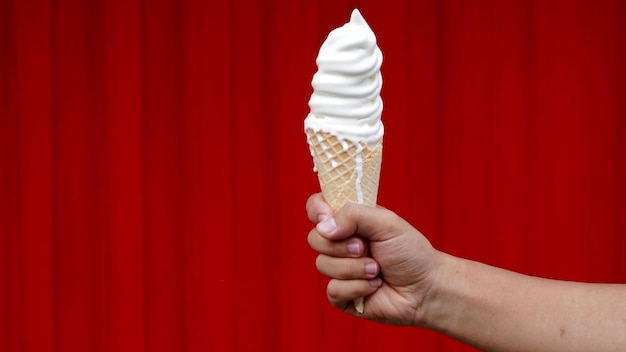 A hand holds a waffle cone with a red background.