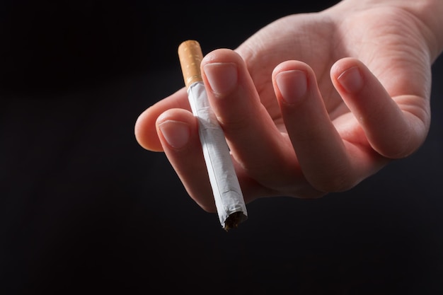 Hand is giving out cigarette on black background