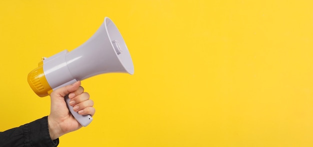 Hand is hold megaphone and wear black shirt on yellow background