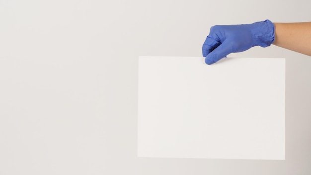 Hand is holding the A4 paper and wear purple latex glove on white background