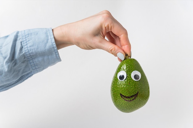 Hand is holding avocado smile over white background Avocado with funny face