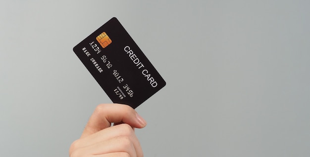 Hand is holding black credit card isolated on grey background.