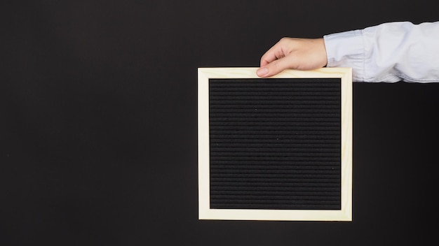 Hand is holding a black letter board on black background