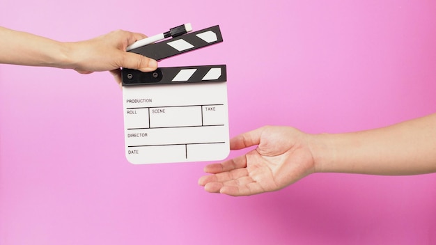 Hand is holding clapper board and marker pen and sending clapperboard to ather hand on pink background