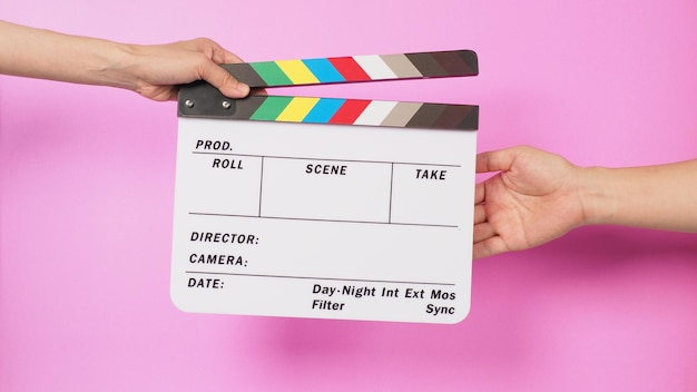 Hand is holding clapper board and sending clapperboard to other hand on pink background