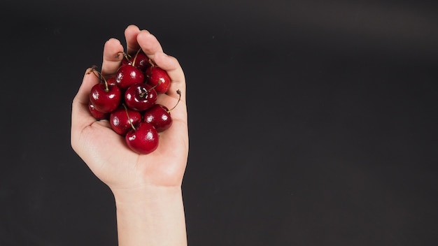 Hand is holding group of cherries on black background.