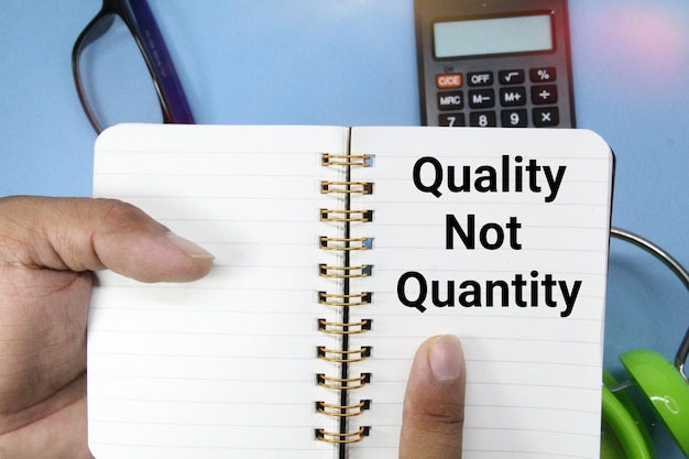 A hand is holding a notebook with the words quality not quantity on it.