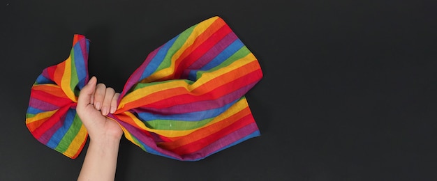 Hand is holding rainbow handkerchief on black background.