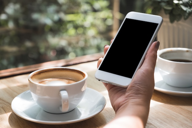 A hand is holding a smartphone, and coffee cups on table