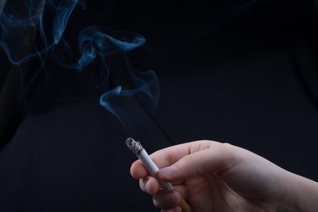 Hand is holding smoking cigarette on black background