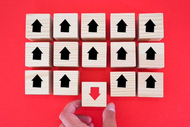 Hand is laying down a wooden block with a red arrow facing the opposite direction of the black arrows. Unique, think different, individual and stand out from the crowd