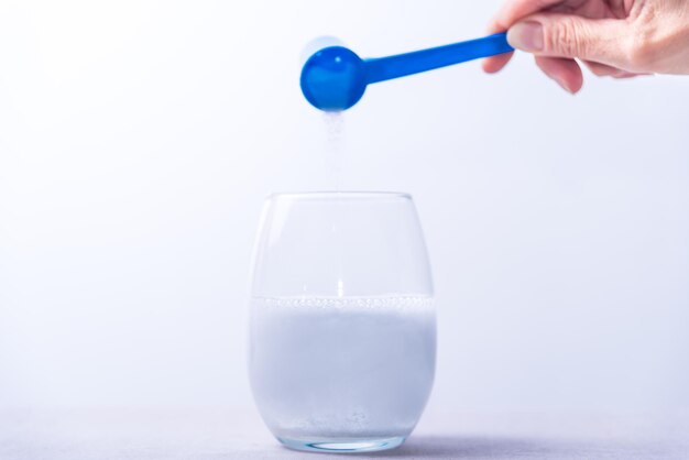 A hand is pouring milk into a glass with a blue spoon.