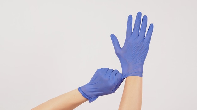 Hand is pulling purple latex gloves on white background