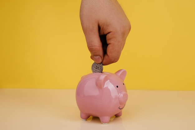 Hand is putting coin into piggy bank Saving money or investment concept