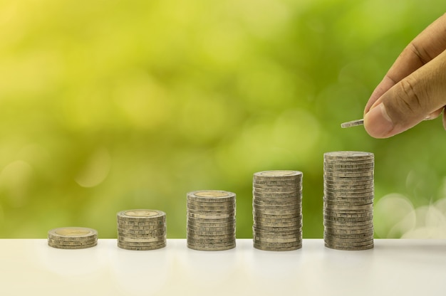 The hand is putting coins and coins accummulate in column that represent money saving or financial planning idea for economy.