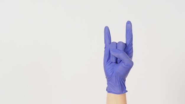 Hand is wear violet or purple glove and doing rock hand sign on white background