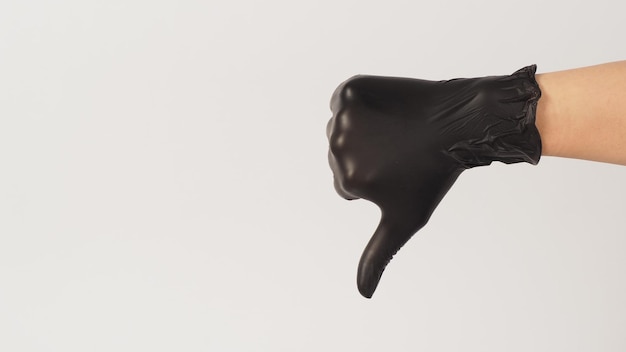 The hand is wearing a black latex glove and do dislike or thumbs down hand sign on white background