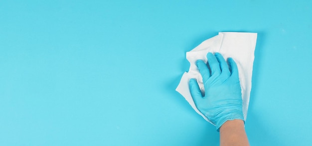 Hand is wiping and hold white crumpled paper tissue on blue background Hand wear blue latex glove