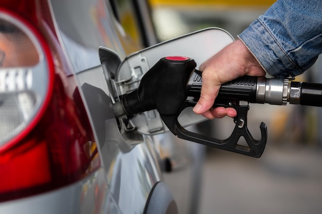 Hand in jeans jacket refueling gray metallic car on gas station closeup with selective focus