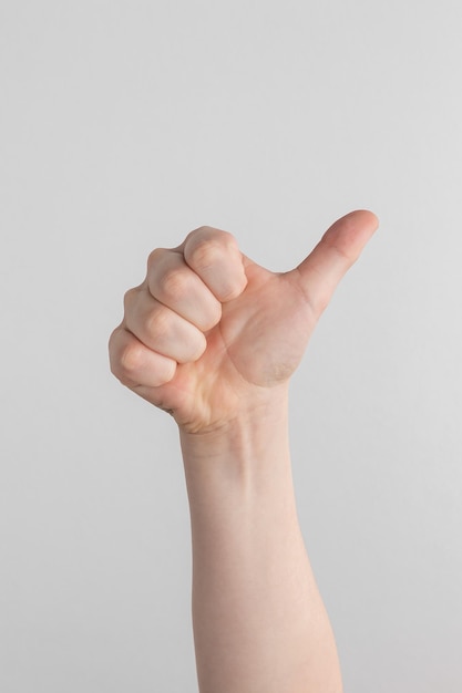 hand of kids showing thumbs up through hole in yellow paper with torn edges against white background