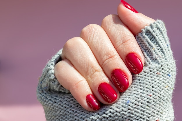 Hand in knitted sweater with burgundy nails