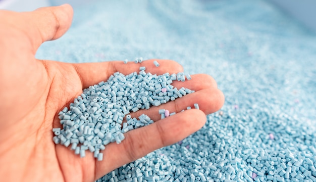 Hand on large pile of blue plastic granules in temporary storage of production line at recycle factory, master batch dye polymer plastics resin pellet