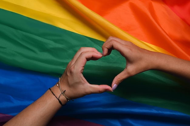 Hand of LGBT women holding together and forming heart shape over rainbow flag Concept of LGBT pride