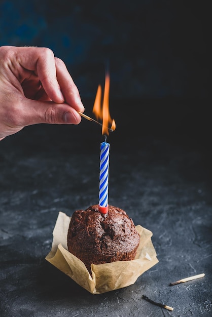 Hand lighting candle with a match on birthday chocolate muffin