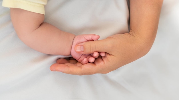 Hand of little baby and finger of adult on white sheet bed background