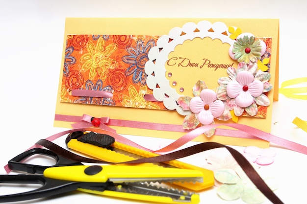 Hand made scrapbooking post card and tools on a white background close-up