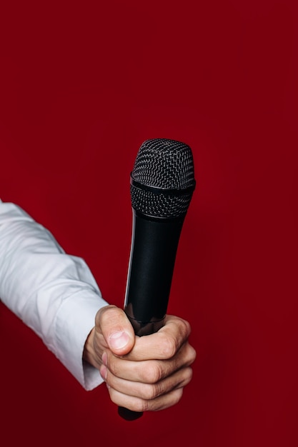 The hand of a male presenter ,reporter, journalist holds a microphone on a red wall