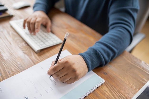 Hand of male teacher or economist with pen pointing at financial document while sitting by table and working