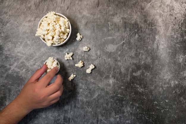 Hand of man eating popcorn, bowls with popcorn and grey background. Weekend or evening plan