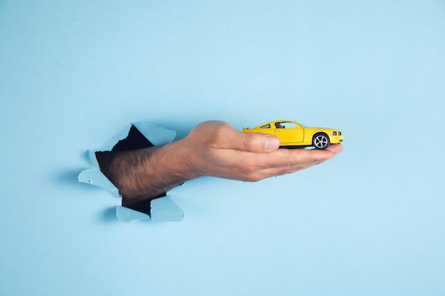 Hand of man hold miniature toy cars on the blue background